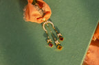 Gold pendant necklace with seed pearls and orange citrine drops on a textured green surface.