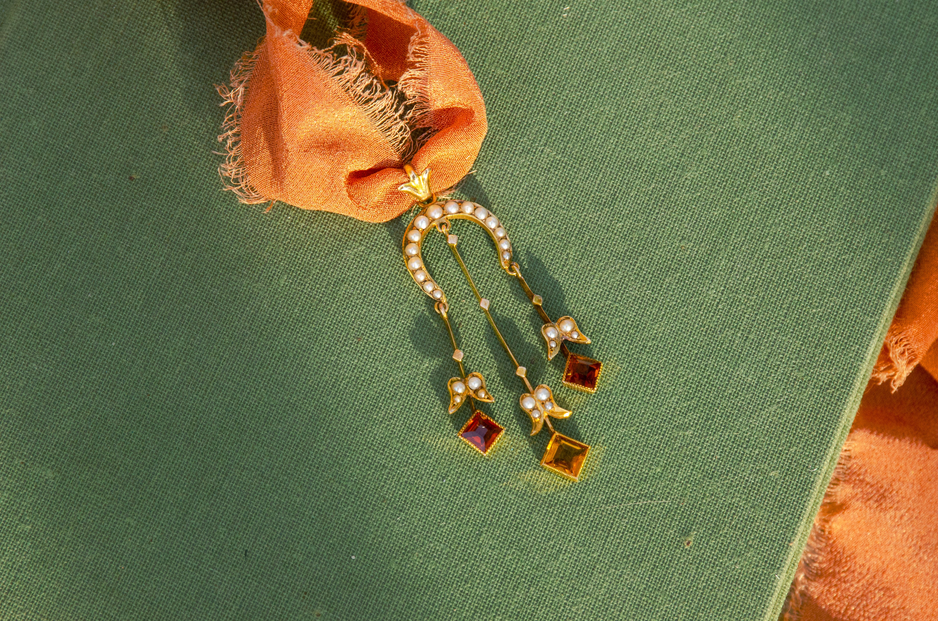 Gold pendant necklace with seed pearls and orange citrine drops on a textured green surface.
