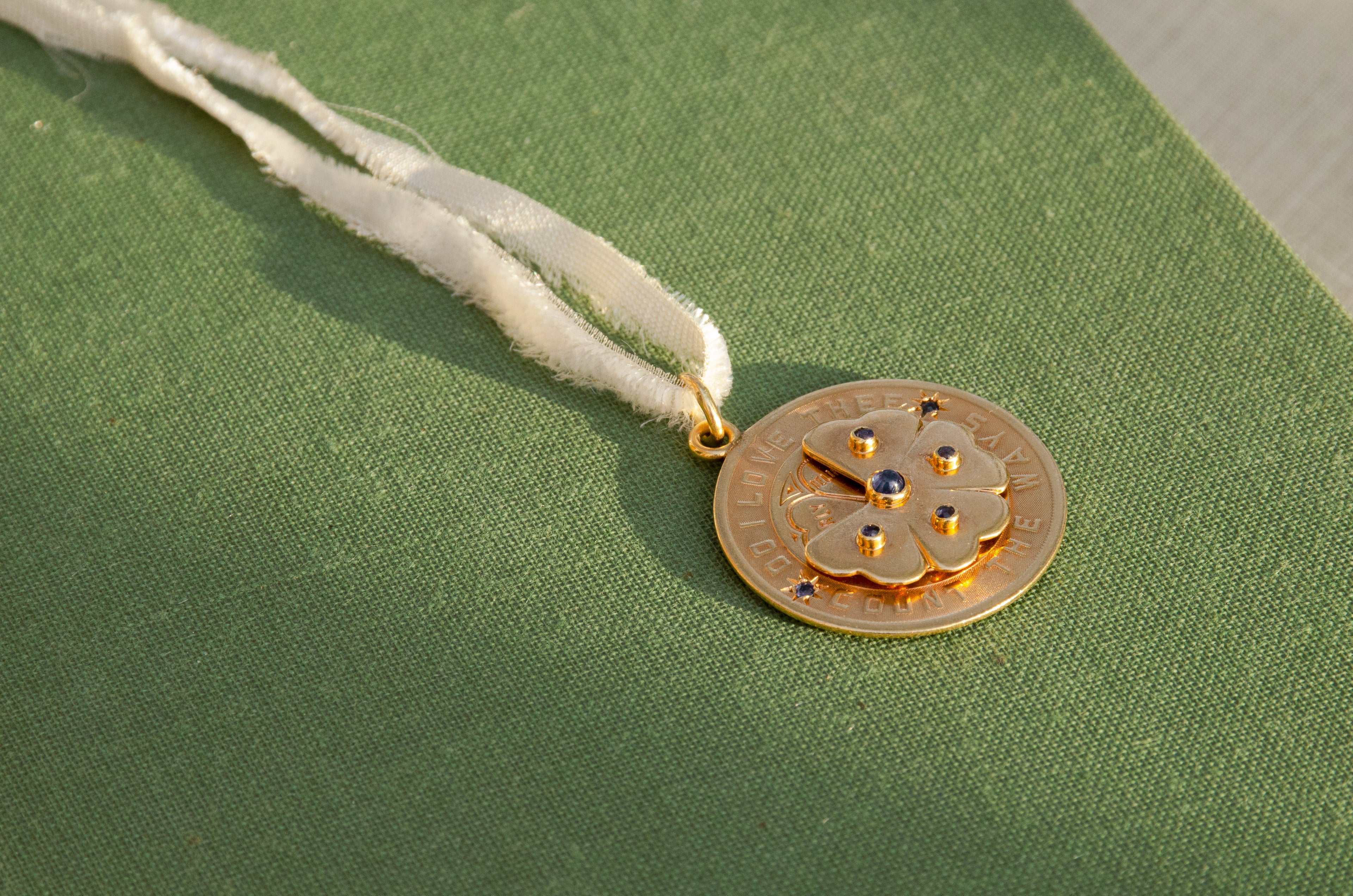 A round gold pendant with a floral design and blue stone accents, resting on a textured green surface.