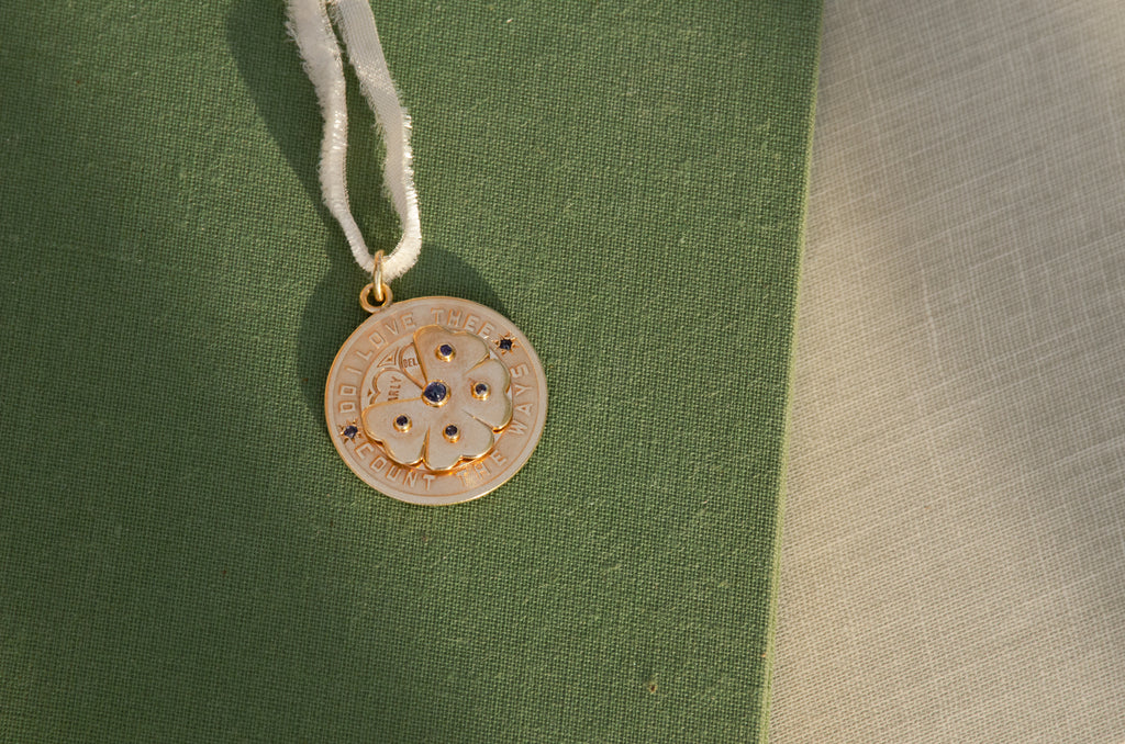 A round gold pendant with a floral design and blue stone accents, resting on a textured green surface.