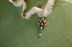 A gold lavalier pendant with seed pearls and a center diamond resting on a green textured surface.