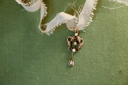 A gold lavalier pendant with seed pearls and a center diamond resting on a green textured surface.