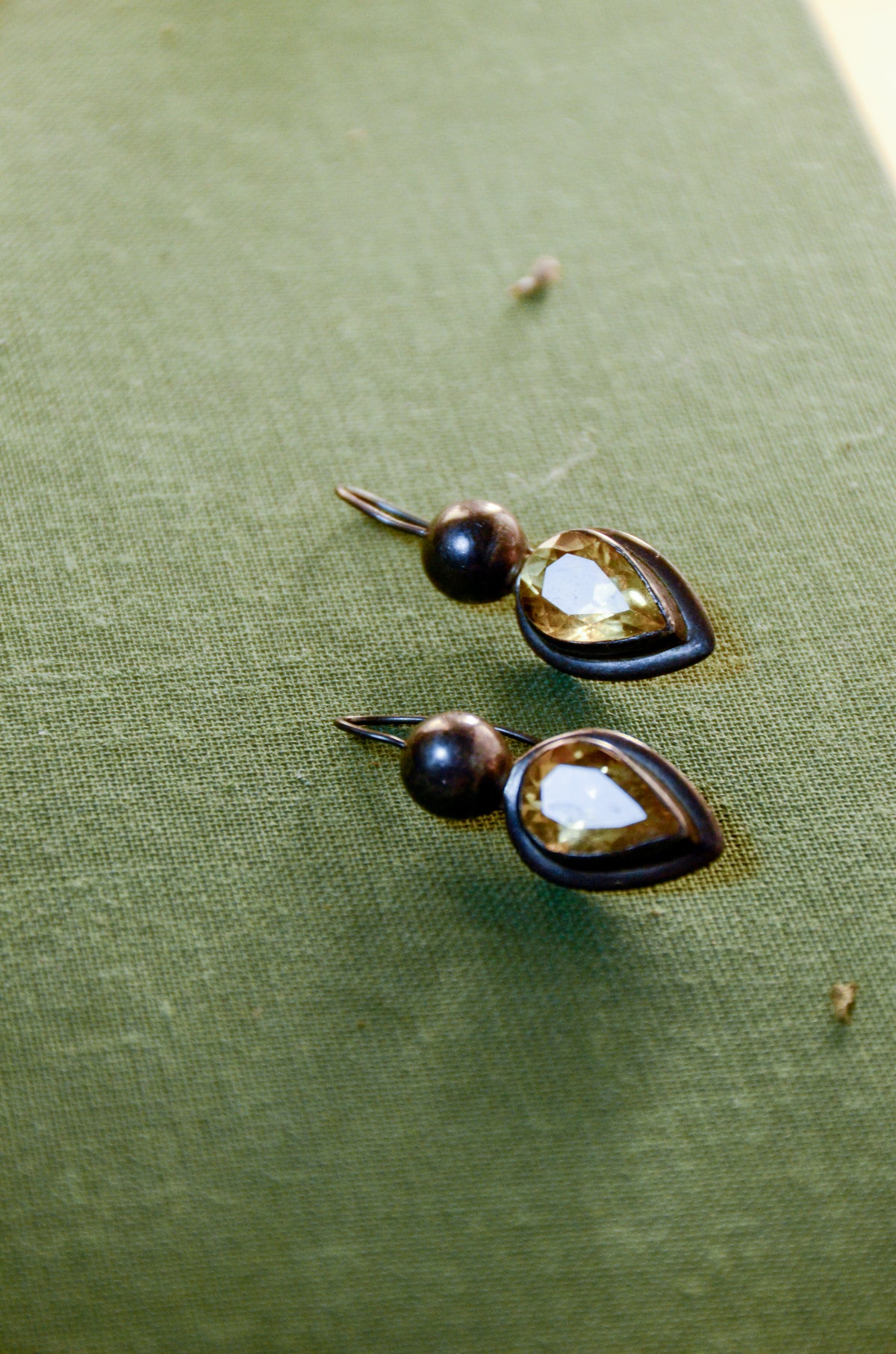 Pair of teardrop dangle earrings with orange citrine stones on a green fabric background