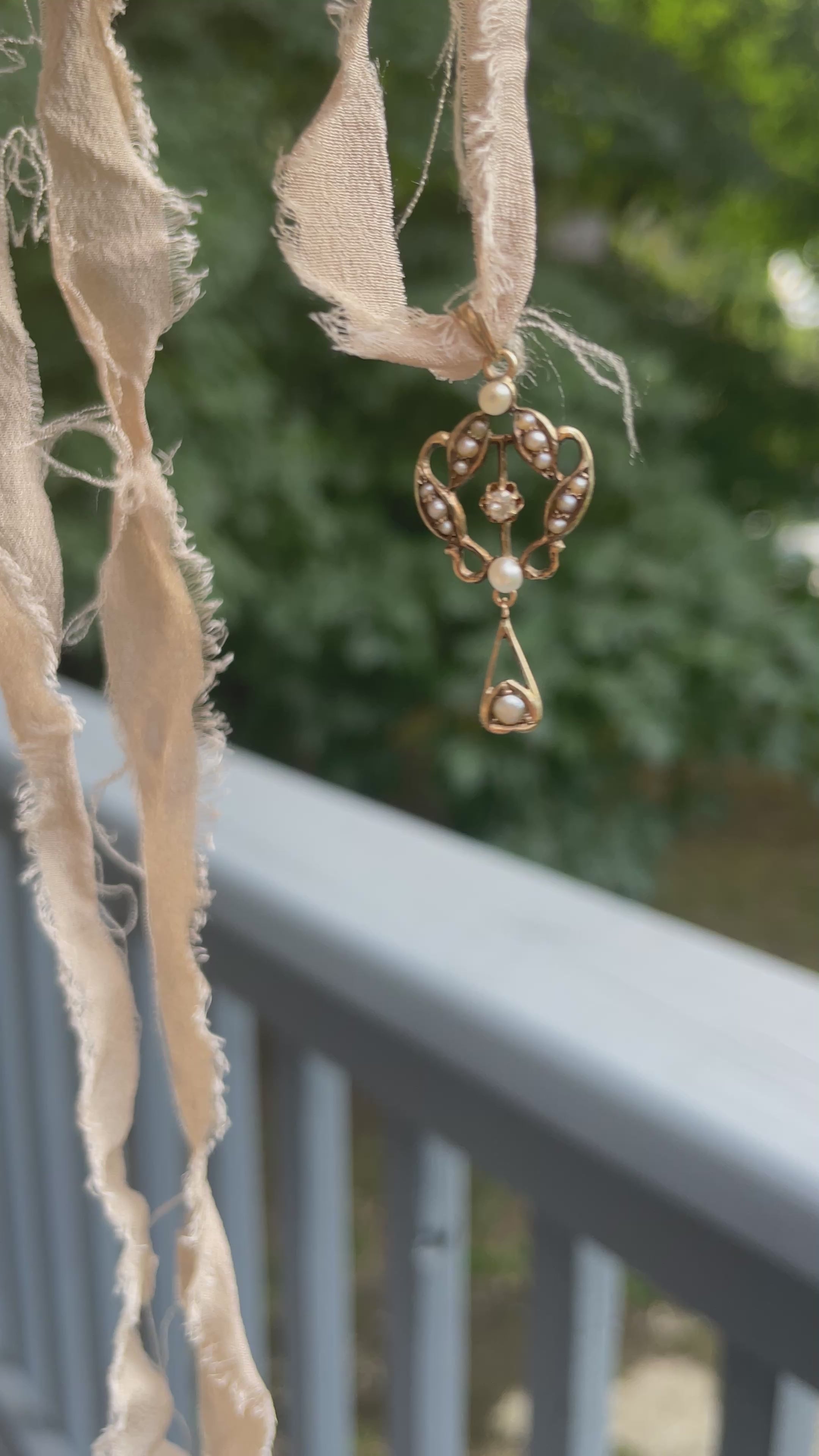 A gold lavalier pendant with seed pearls and a center diamond swaying on a beige silk ribbon.