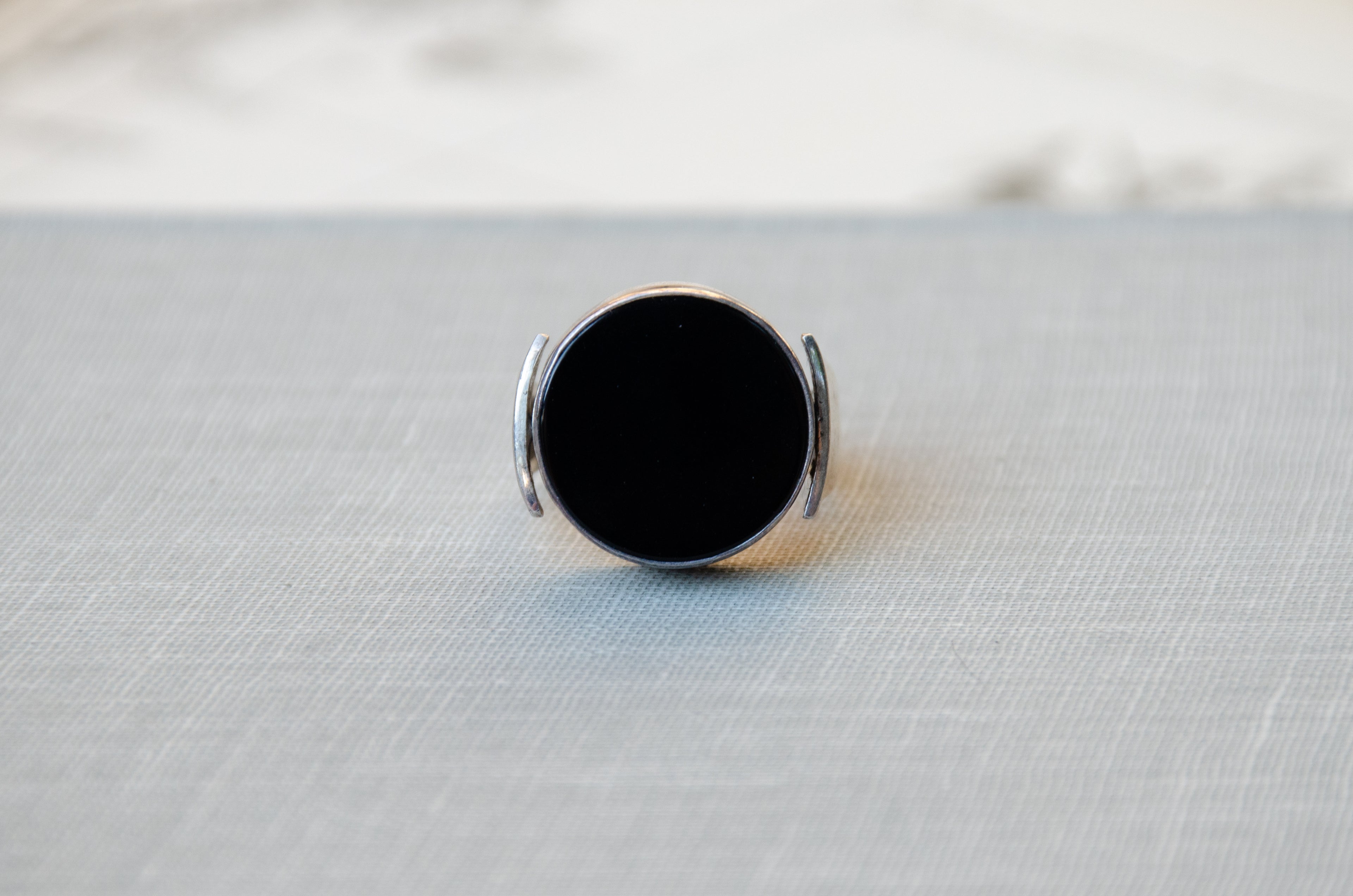 A sterling silver ring with a large, round, matte obsidian black face, resting on a textured light gray surface.