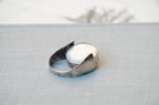 A silver ring with a large, smooth white oval mother of pearl stone, resting on a textured light gray fabric surface.